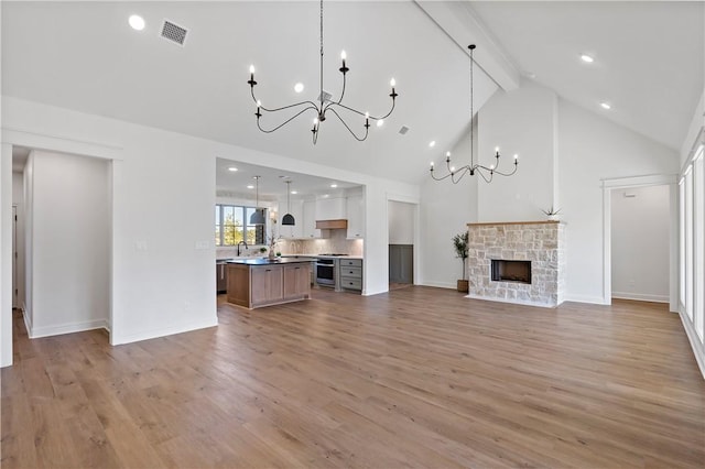 unfurnished living room with beam ceiling, an inviting chandelier, light hardwood / wood-style flooring, high vaulted ceiling, and a fireplace