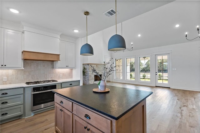 kitchen featuring pendant lighting, decorative backsplash, light wood-type flooring, appliances with stainless steel finishes, and white cabinetry