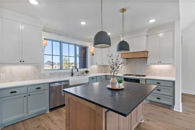 kitchen with appliances with stainless steel finishes, pendant lighting, white cabinets, light hardwood / wood-style floors, and a kitchen island