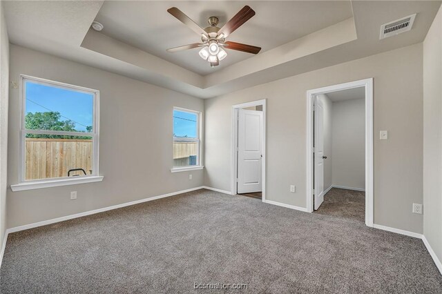 unfurnished bedroom featuring ceiling fan, a tray ceiling, and carpet floors