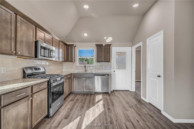 kitchen with appliances with stainless steel finishes, lofted ceiling, sink, backsplash, and light wood-type flooring