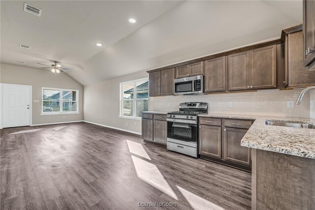 kitchen with sink, appliances with stainless steel finishes, dark brown cabinets, light stone countertops, and vaulted ceiling