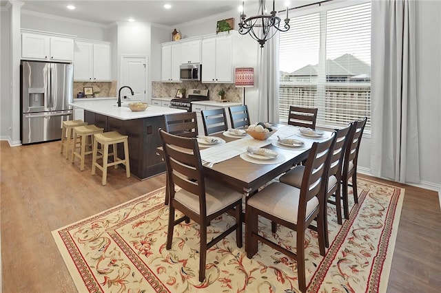 dining area with ornamental molding, light wood-type flooring, sink, and an inviting chandelier