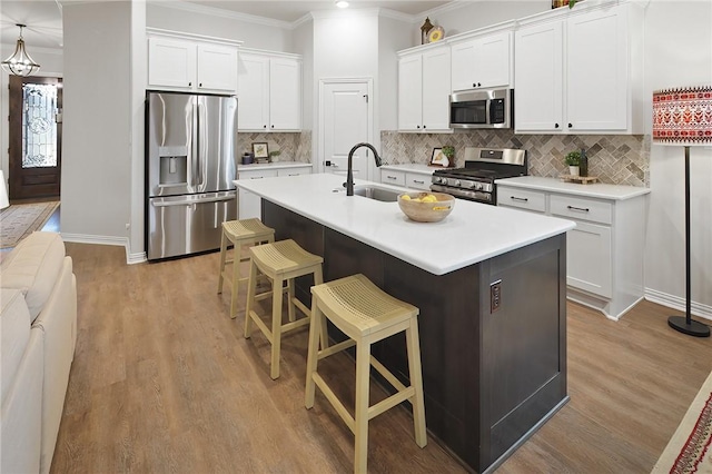 kitchen featuring a breakfast bar area, white cabinetry, crown molding, stainless steel appliances, and a kitchen island with sink