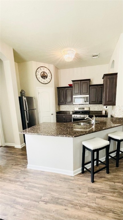 15481 Baker Meadow Loop, College Station, TX 77845 - kitchen with stainless steel appliances, dark stone counters, a sink, a breakfast bar, and light wood-style floors
