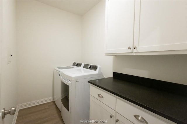 clothes washing area with washer and dryer, dark wood-type flooring, and cabinets