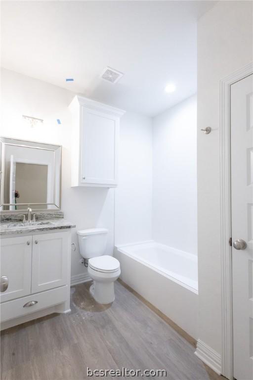 full bathroom with hardwood / wood-style flooring, vanity, toilet, and washtub / shower combination