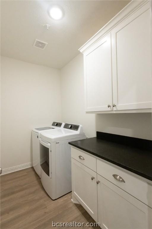 clothes washing area featuring cabinets, light hardwood / wood-style floors, and washer and clothes dryer