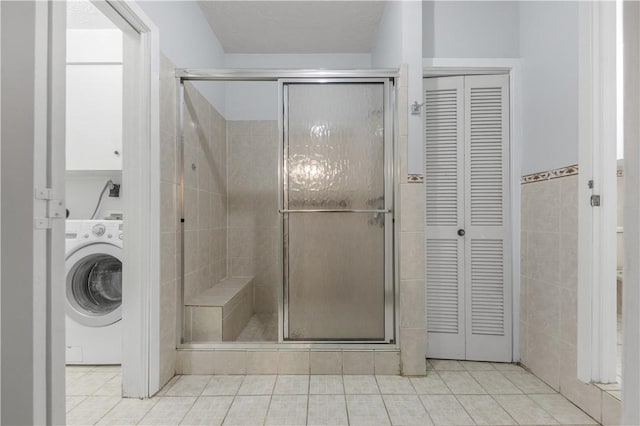 bathroom featuring tile patterned floors, washer / clothes dryer, a shower with door, and tile walls