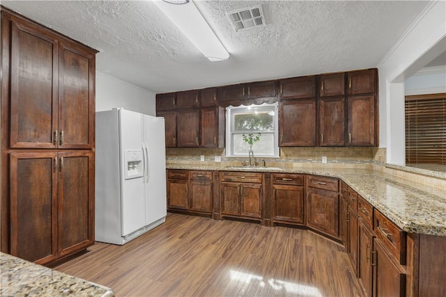 kitchen with light stone countertops, white fridge with ice dispenser, sink, and light hardwood / wood-style flooring