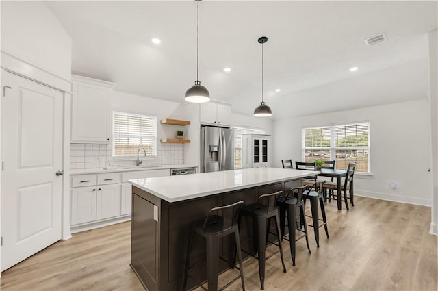 kitchen with a sink, stainless steel fridge with ice dispenser, light countertops, a kitchen island, and visible vents
