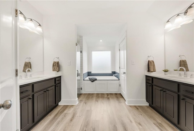 full bath with a sink, a stall shower, wood finished floors, and two vanities