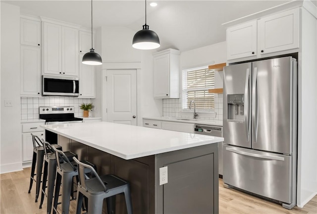 kitchen featuring appliances with stainless steel finishes, a sink, light wood-style floors, a center island, and tasteful backsplash