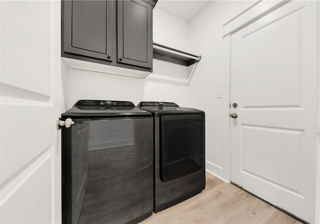 laundry area featuring light wood-type flooring, washer and clothes dryer, and cabinet space