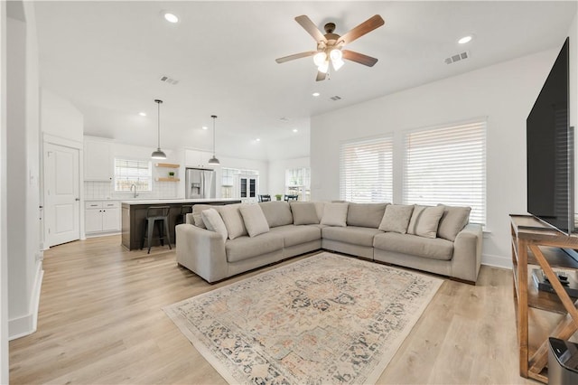 living room with visible vents, light wood-style floors, ceiling fan, and a wealth of natural light