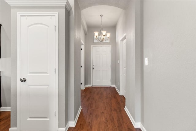 hallway with a chandelier, arched walkways, dark wood-style flooring, and baseboards