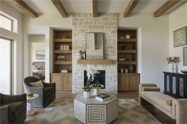 living room with a stone fireplace, built in shelves, beamed ceiling, and dark wood-type flooring