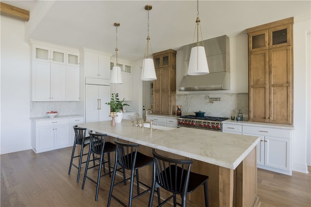 kitchen featuring a large island, wall chimney exhaust hood, decorative backsplash, white cabinets, and light wood-type flooring