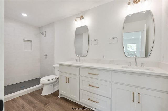 bathroom with tiled shower, vanity, hardwood / wood-style flooring, and toilet