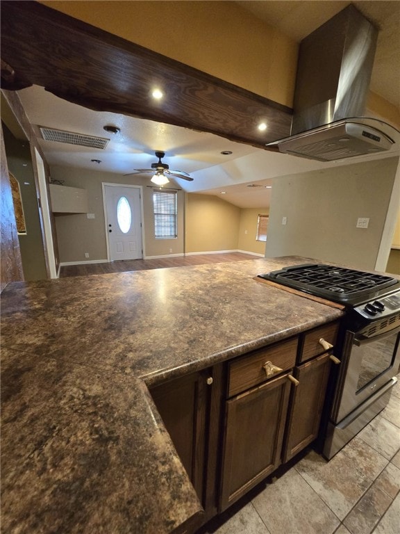 kitchen featuring wall chimney range hood, high end stainless steel range, ceiling fan, light tile patterned floors, and dark brown cabinetry