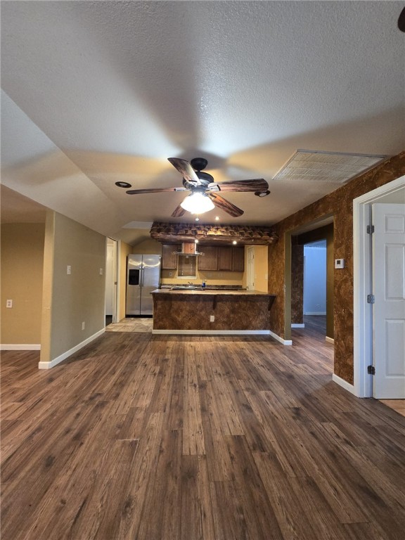 unfurnished living room with a textured ceiling, ceiling fan, dark wood-type flooring, and vaulted ceiling