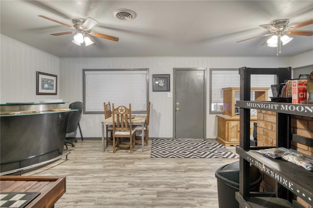 interior space with ceiling fan, light hardwood / wood-style floors, and wood walls