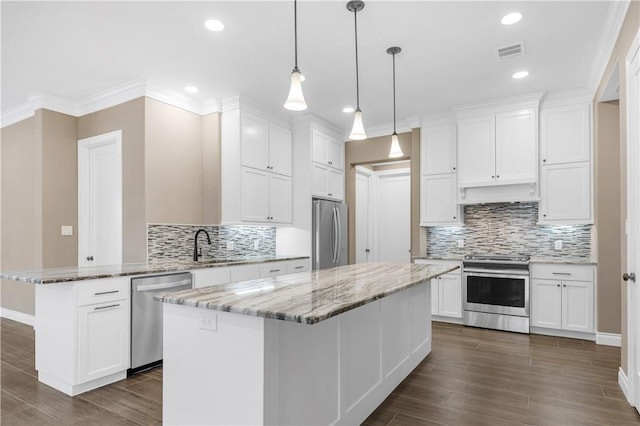 kitchen with light stone countertops, appliances with stainless steel finishes, pendant lighting, white cabinets, and a kitchen island