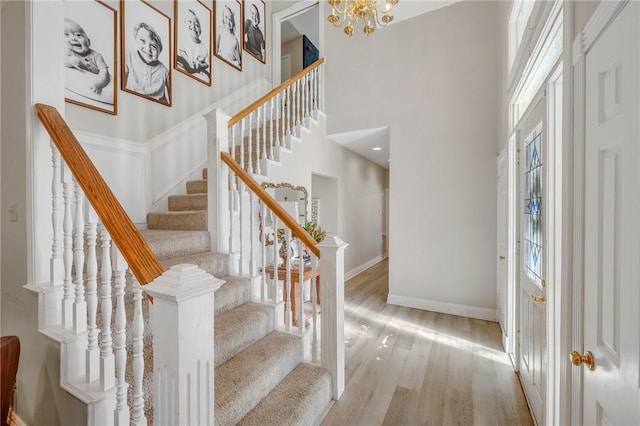 staircase featuring a notable chandelier, wood-type flooring, and a high ceiling