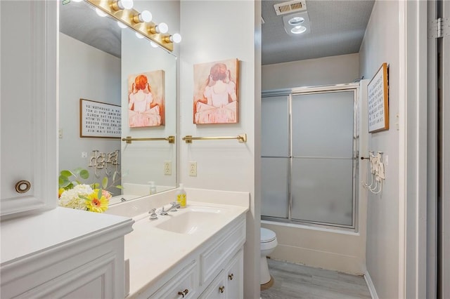 full bathroom featuring hardwood / wood-style floors, vanity, bath / shower combo with glass door, toilet, and a textured ceiling