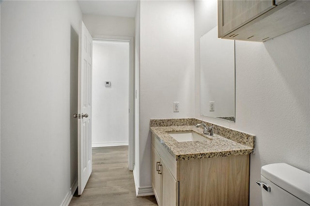 half bath with vanity, wood finished floors, toilet, and baseboards