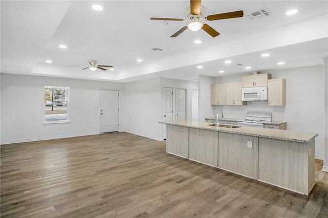 kitchen featuring a raised ceiling, visible vents, an island with sink, wood finished floors, and white appliances