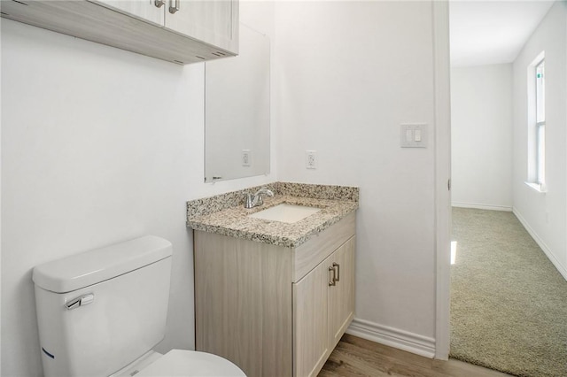 bathroom featuring toilet, baseboards, wood finished floors, and vanity