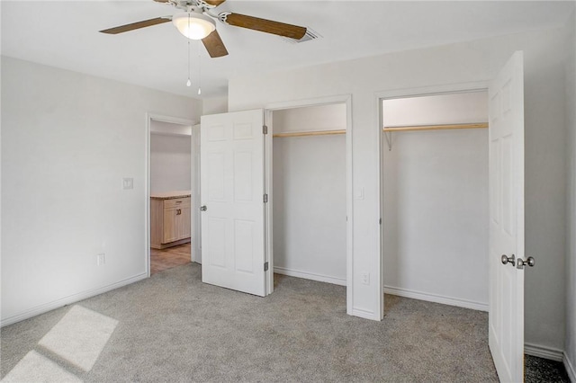 unfurnished bedroom with light carpet, ceiling fan, baseboards, and two closets