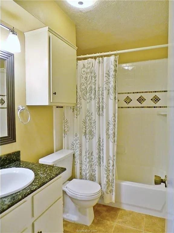 full bathroom featuring tile patterned flooring, a textured ceiling, toilet, shower / bath combo with shower curtain, and vanity