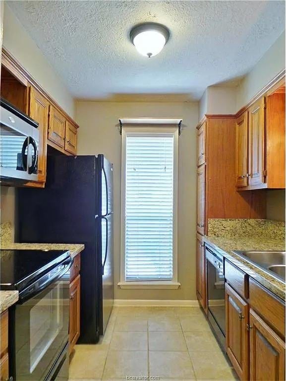 kitchen featuring light stone countertops, light tile patterned floors, a textured ceiling, and appliances with stainless steel finishes