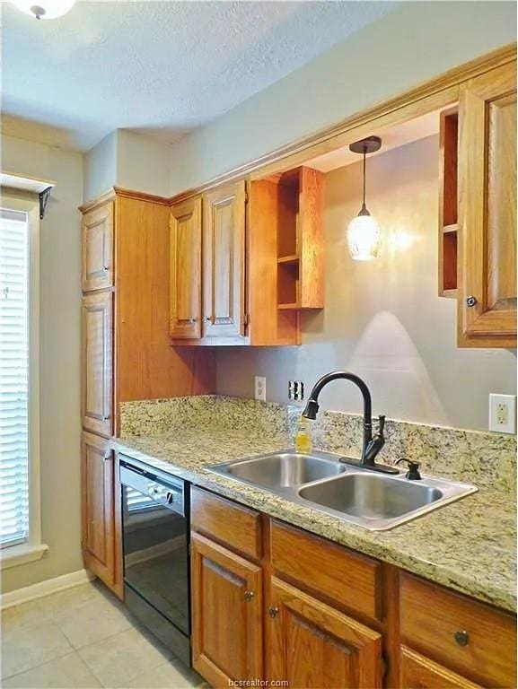 kitchen with a textured ceiling, sink, light tile patterned floors, decorative light fixtures, and black dishwasher