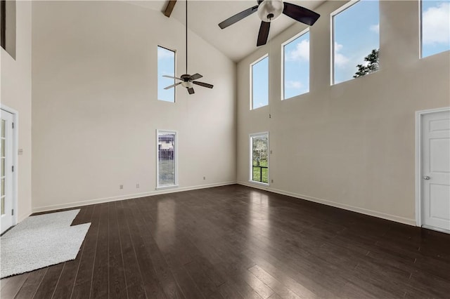 unfurnished living room with ceiling fan, beamed ceiling, a towering ceiling, and dark hardwood / wood-style floors