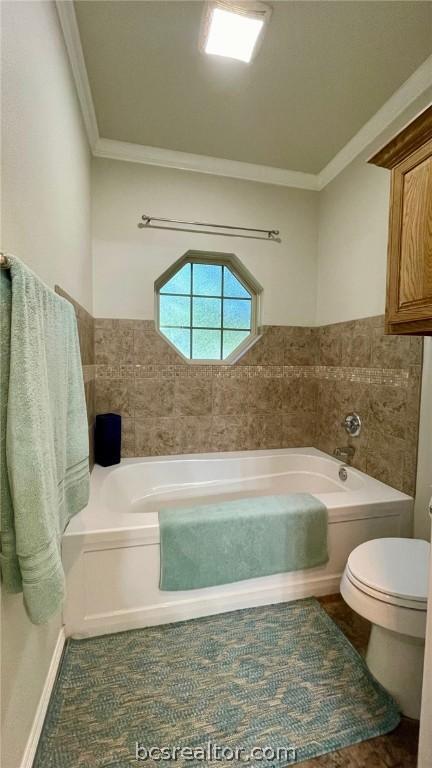 bathroom featuring toilet, ornamental molding, a tub to relax in, and tile walls