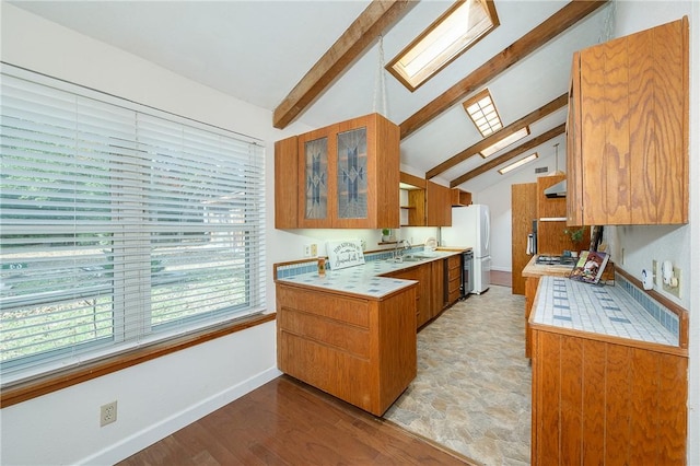 kitchen with white fridge, sink, vaulted ceiling with skylight, and light wood-type flooring