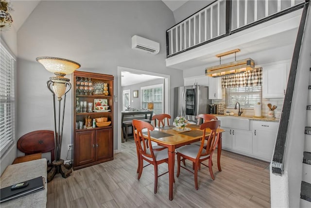 dining space featuring light hardwood / wood-style floors, sink, high vaulted ceiling, and a wall mounted air conditioner