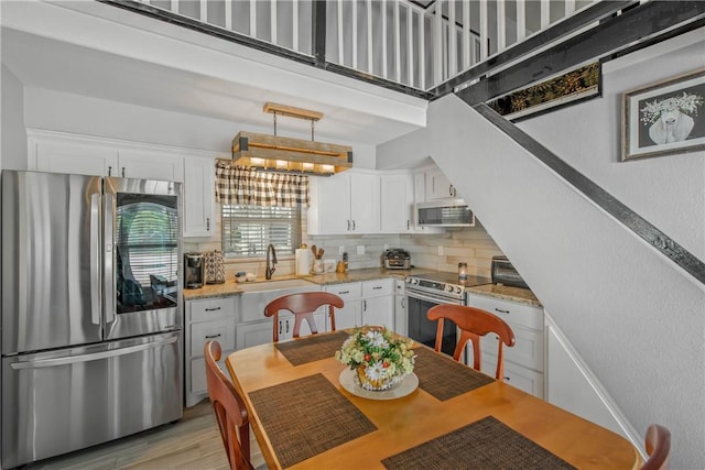 kitchen with pendant lighting, sink, white cabinetry, light stone counters, and stainless steel appliances