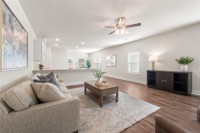 living room with wood-type flooring, ceiling fan with notable chandelier, and sink