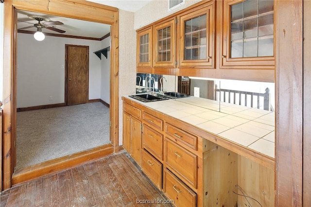 kitchen with ceiling fan, crown molding, sink, dark wood-type flooring, and tile counters