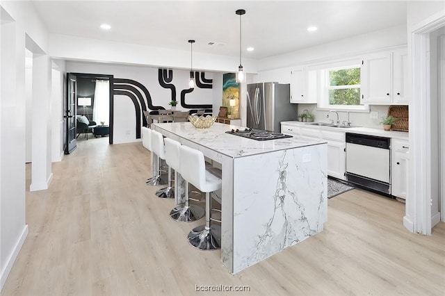 kitchen with pendant lighting, white cabinets, sink, a kitchen island, and stainless steel appliances