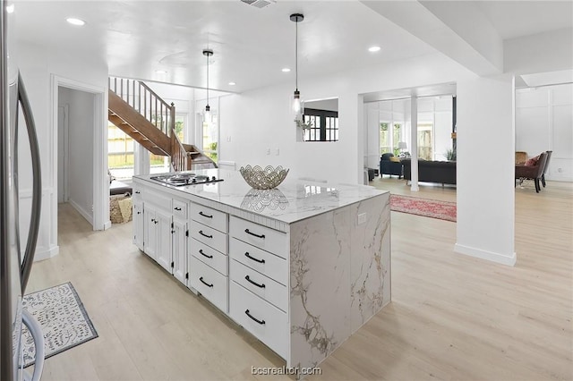 kitchen with white cabinets, light wood-type flooring, decorative light fixtures, a kitchen island, and stainless steel appliances