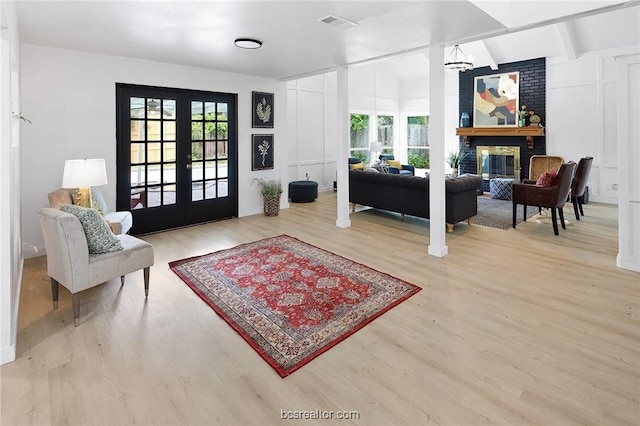 living room with a fireplace, french doors, lofted ceiling with beams, and light wood-type flooring