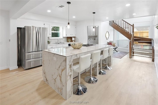 kitchen featuring pendant lighting, white cabinetry, stainless steel refrigerator, and light hardwood / wood-style flooring