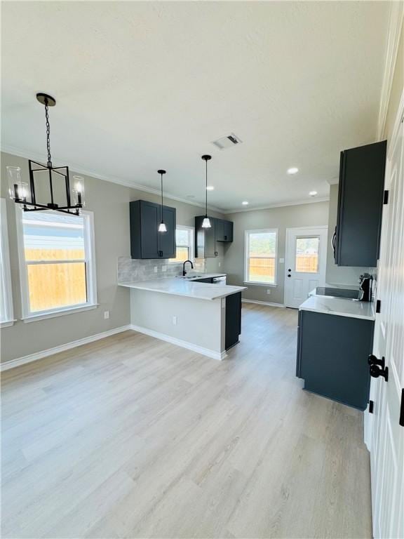 kitchen with kitchen peninsula, ornamental molding, decorative light fixtures, an inviting chandelier, and light hardwood / wood-style flooring