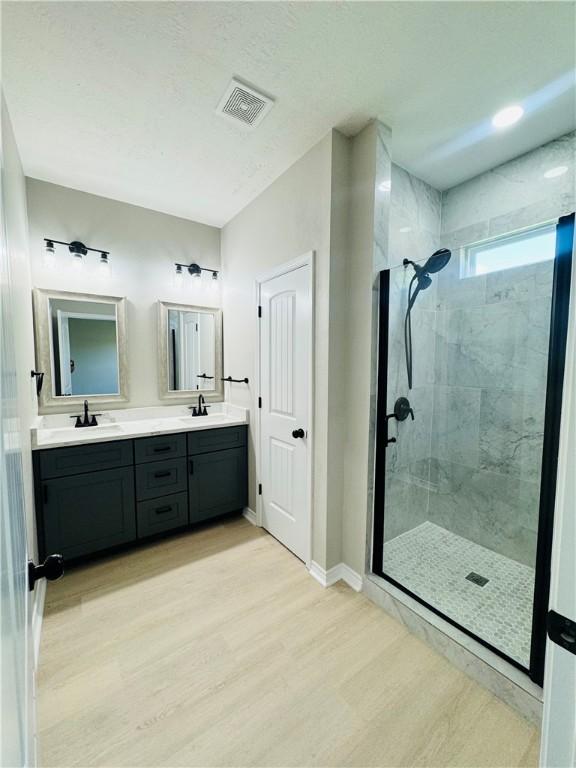 bathroom with tiled shower, wood-type flooring, and vanity