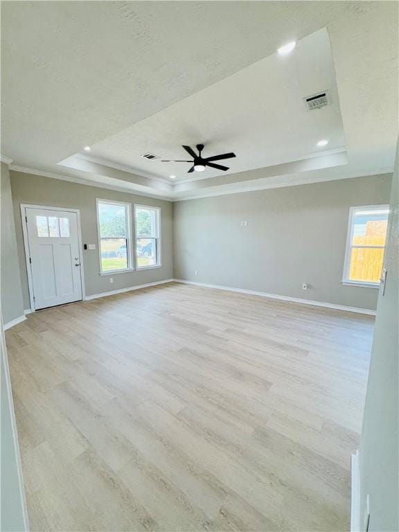 empty room with a raised ceiling, crown molding, a healthy amount of sunlight, and light hardwood / wood-style floors